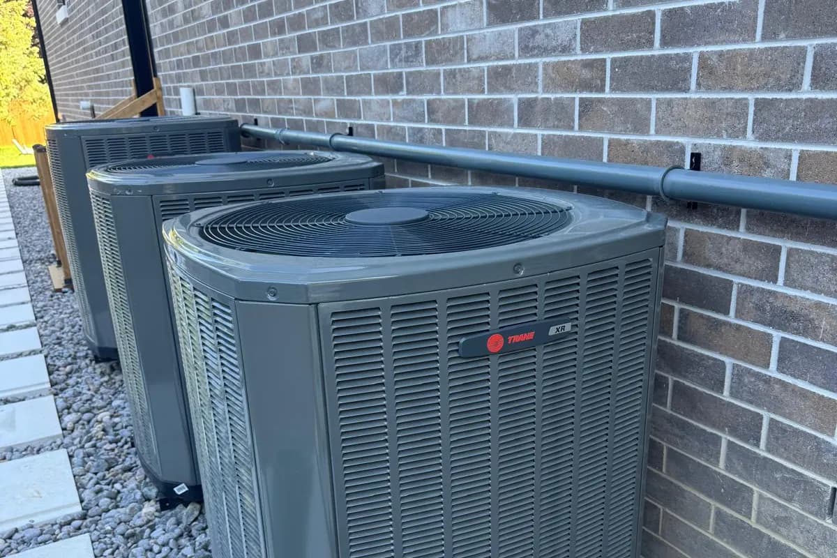 Outdoor HVAC condenser units lined up against a brick wall